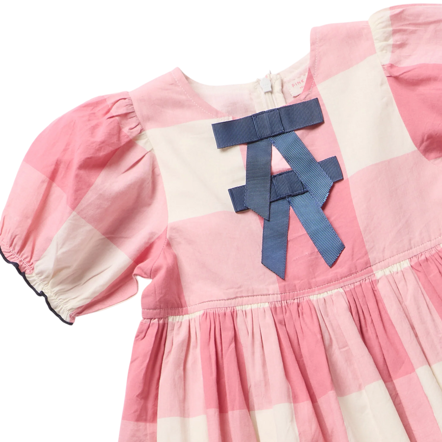 Pink and off-white checkered baby dress with a large blue ribbon bow on the chest, featuring puffed short sleeves and a gathered skirt.