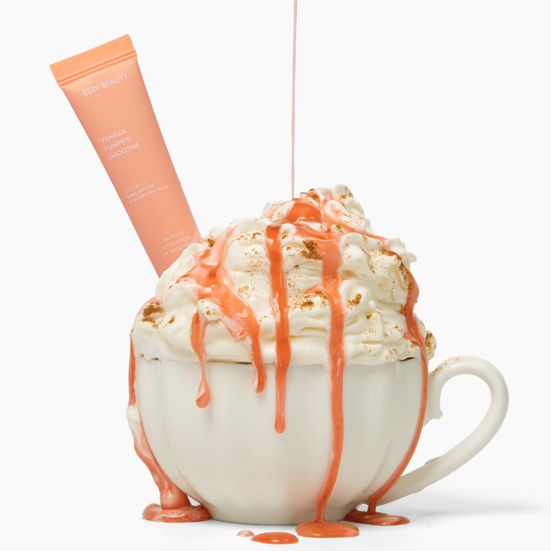 White mug filled with popcorn and whipped cream, drizzled with orange sauce, on a white background.