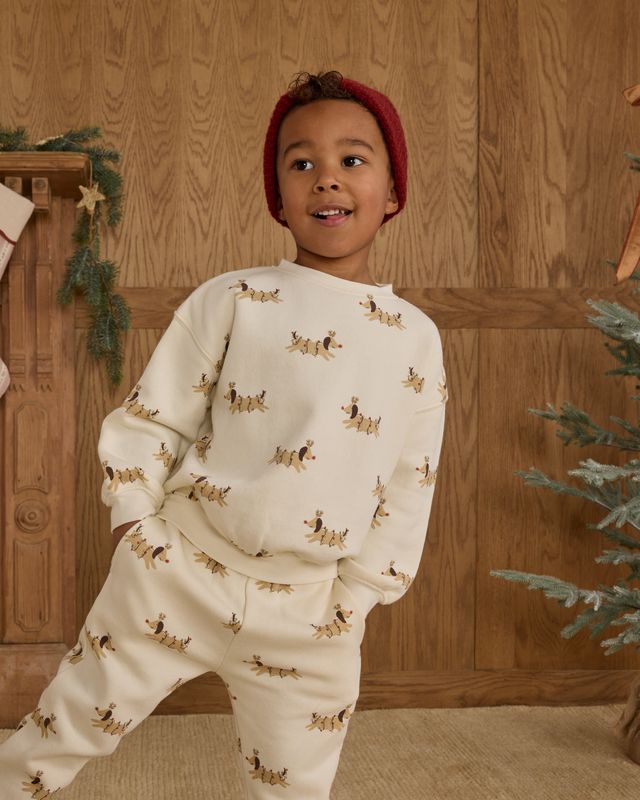 Child wearing a cream-colored sweat set with christmas dog print in a festive room.