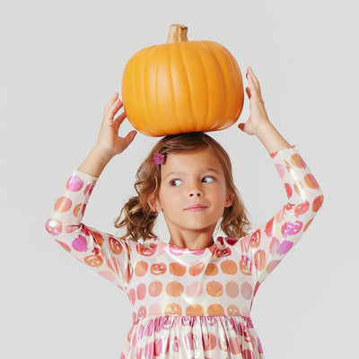 little girls dress with pumpkins all over it. little girl is modeling it holding a giant pumpkin on her head. 