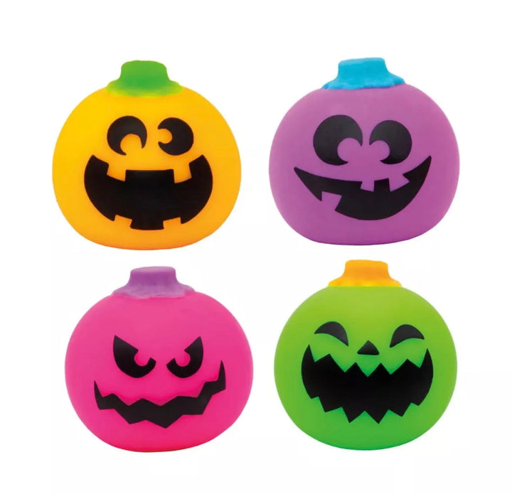 Four colorful pumpkin-shaped squishy toys arranged in a 2x2 grid on a white background. The top-left toy is yellow with a green top and a black jack-o'-lantern face.