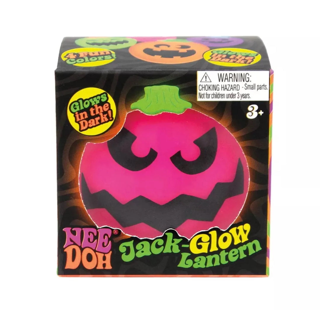 A boxed Nee Doh Glow Jack Lantern toy on a plain white background. The packaging shows a large pink jack-o'-lantern face with a green top, Halloween graphics, and warning text for choking hazards.