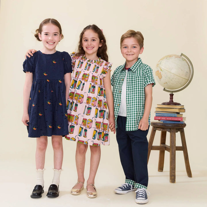 Three children standing together with a world map and books in the background