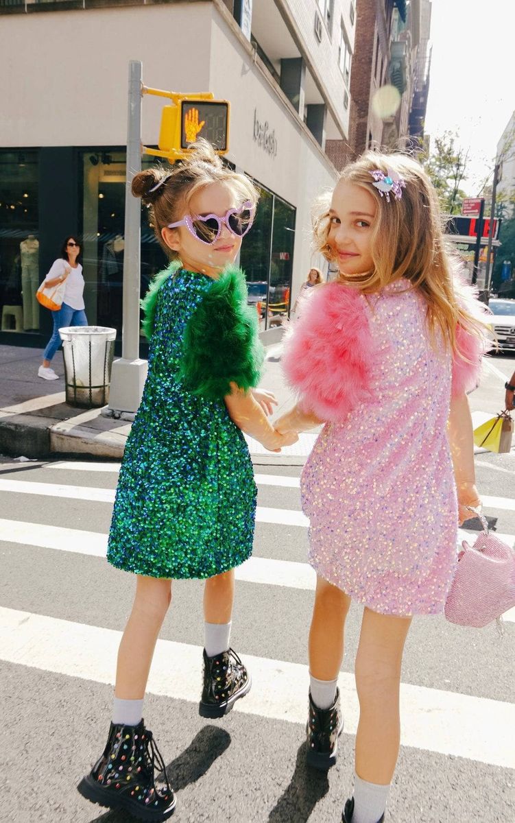 Two young girls in colorful sequin dresses crossing a street.