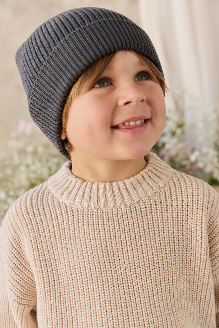 Child wearing a gray knit hat and beige sweater with a blurred floral background