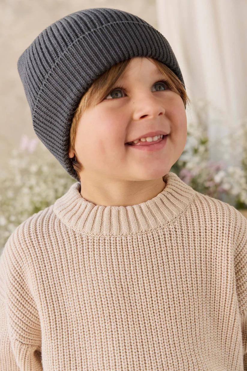 Child wearing a gray knit hat and beige sweater with a blurred floral background
