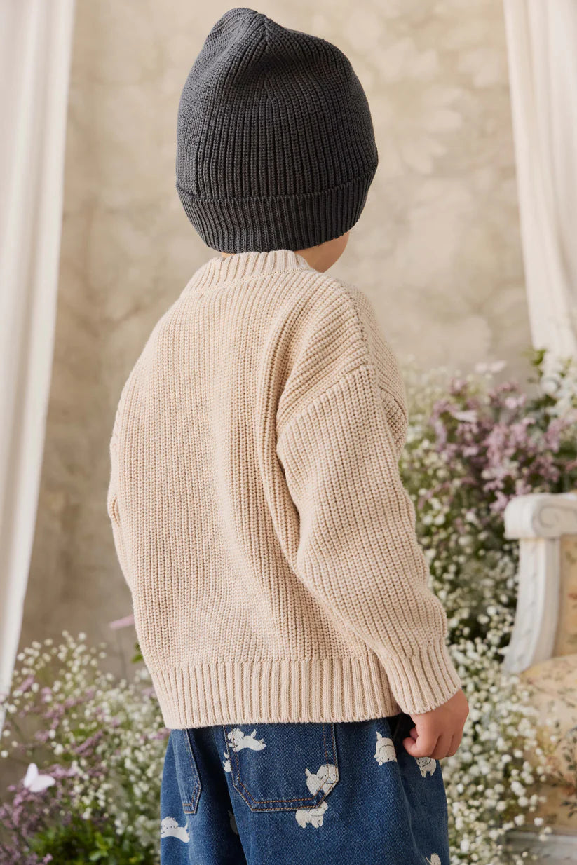 Child wearing a beige knitted sweater and dark knit hat in a garden setting
