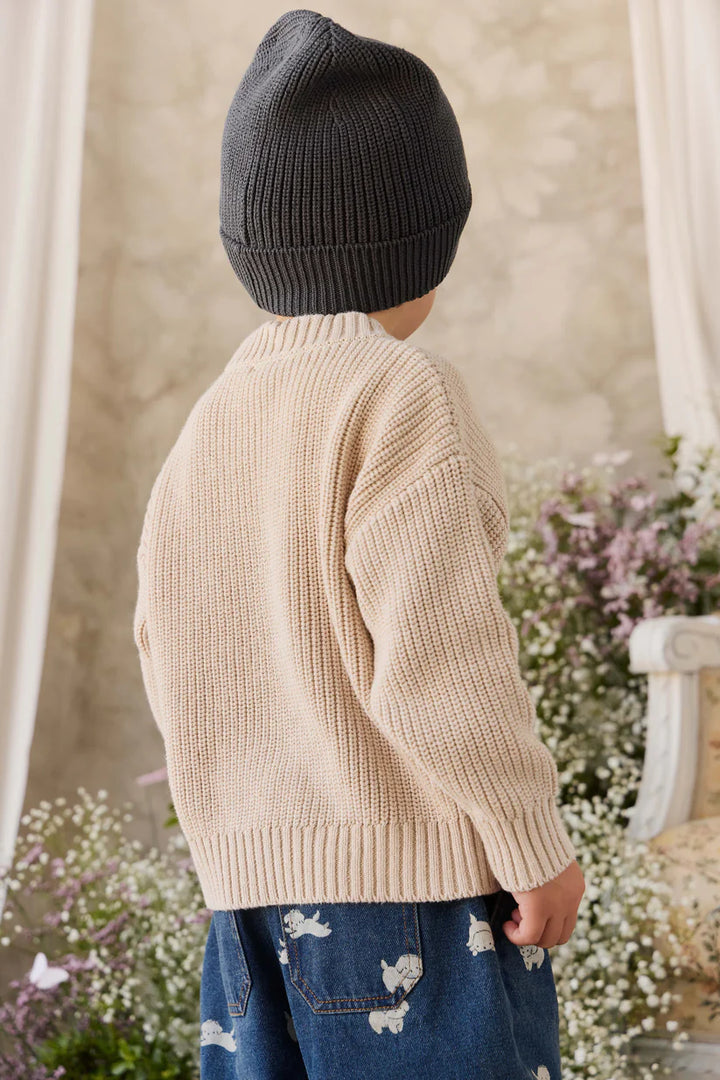 Child wearing a beige knitted sweater and dark knit hat in a garden setting