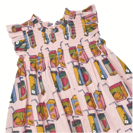 A pink sleeveless dress with a smocked bodice and ruffled neckline, featuring an all-over colorful print of juice boxes with fruit illustrations, shown against a plain white background.