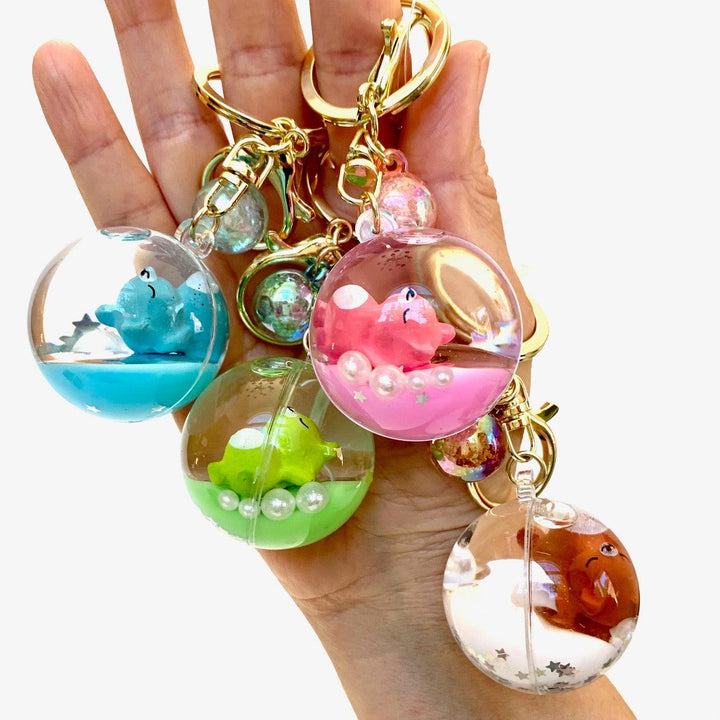 Hand holding a keychain with colorful ball charms featuring different animals on a white background