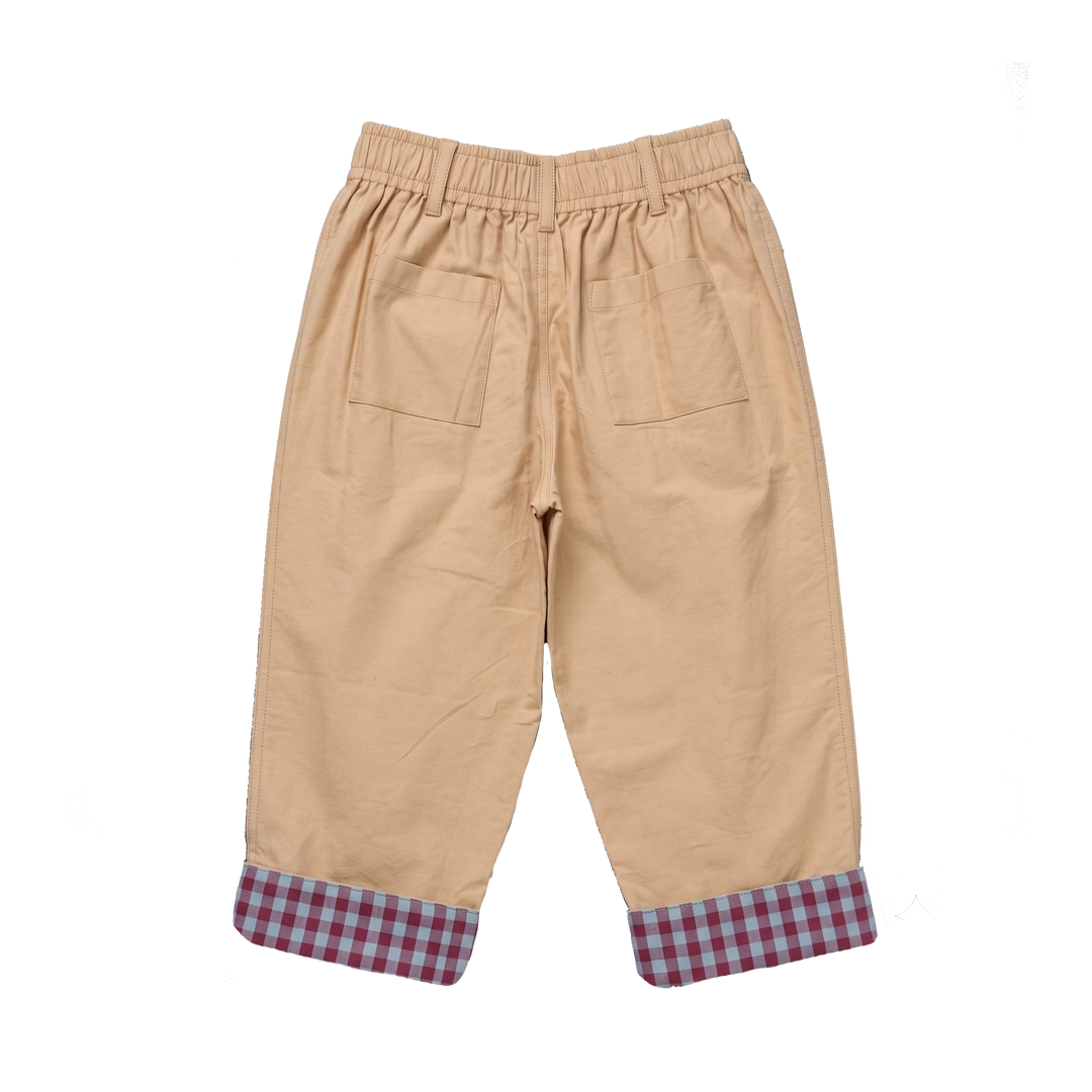 A pair of beige  pants with an elastic waistband, two back patch pockets, and rolled cuffs showing a red and blue gingham pattern, photographed on a solid white background.