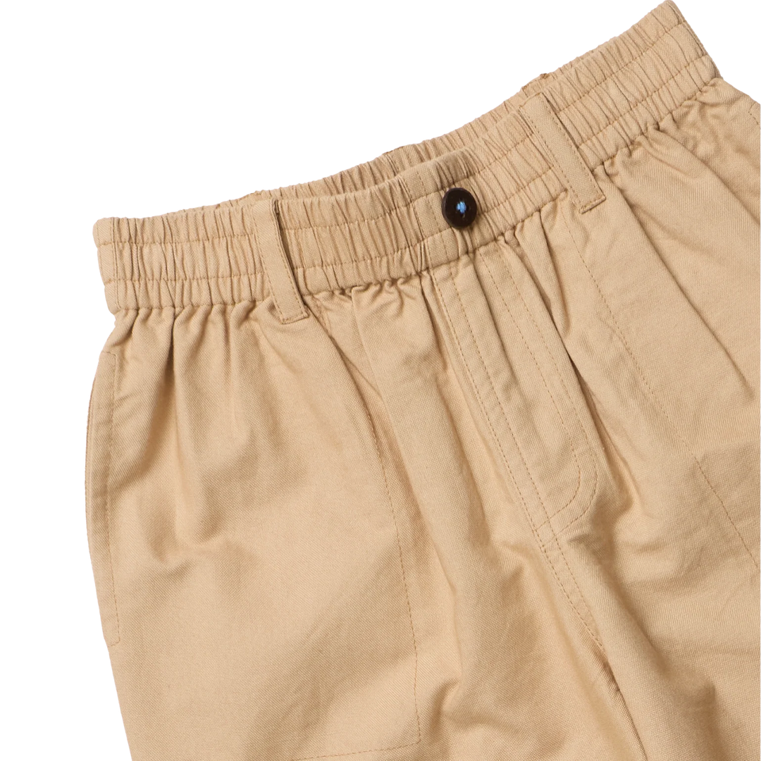 Close-up of tan pleated trousers showing the elastic waistband, a dark button, and the fabric texture against a plain white background.