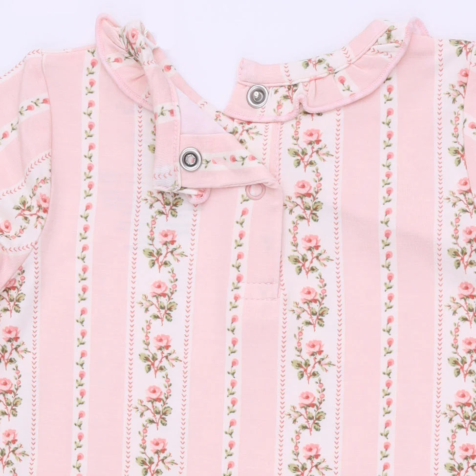 A close-up of a baby garment featuring vertical pink stripes and delicate pink rose floral prints with green leaves, accented by a ruffled collar and snap buttons.