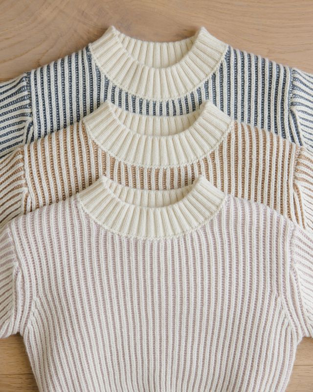 Three knitted sweaters with different color patterns on a wooden surface