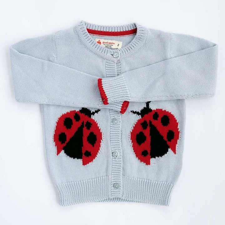 A light blue knit cardigan sweater for children, featuring two large red and black ladybug motifs knitted onto the front. The cardigan has a round neckline, snap-button closure, and red and white striped trim at the collar and cuffs.