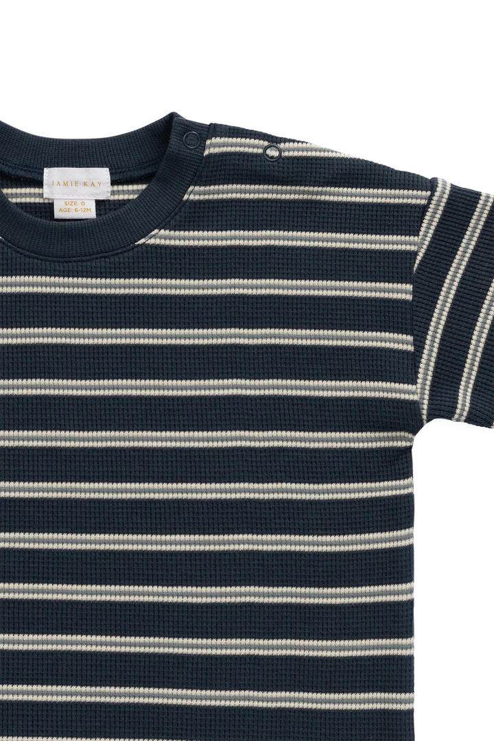 A close-up of a short-sleeve waffle-knit top with horizontal navy and off-white stripes, featuring a ribbed crew neck and a visible J.K