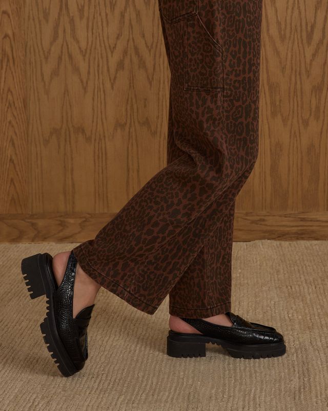 Person wearing brown leopard print pants and black shoes on a wooden floor.