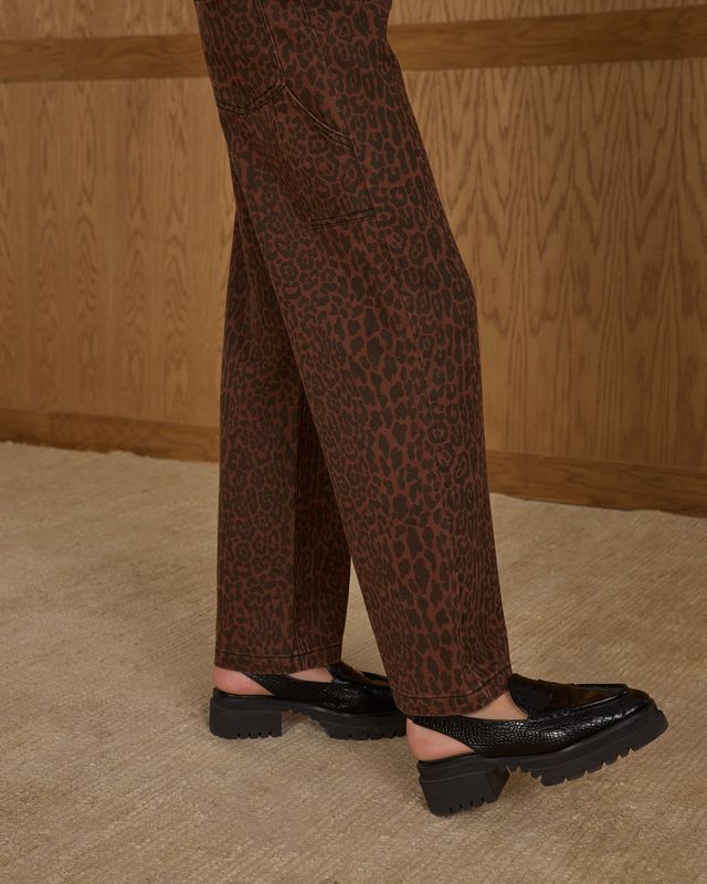 Person wearing leopard print pants and black shoes on a wooden floor.