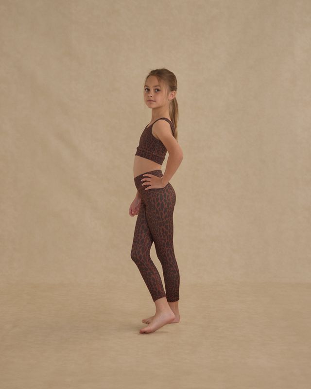 Young girl wearing a leaopard patterned  legging and matching sports bra outfit on a beige background