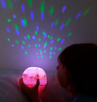 picture of the projector, projecting stars onto the wall in the dark.  The projector base lights up pink and the stars are blue and green