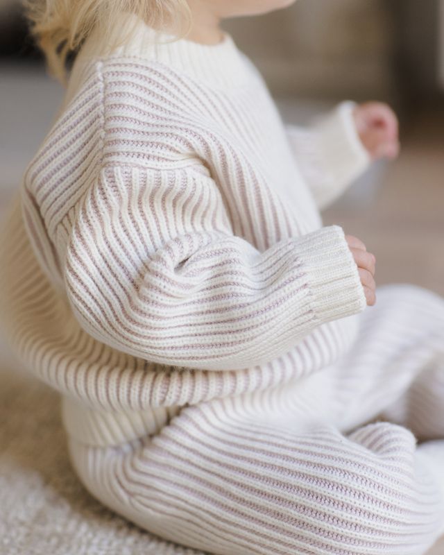 Child wearing a ontrast ribbed knit sweater and pants sitting on the floor.