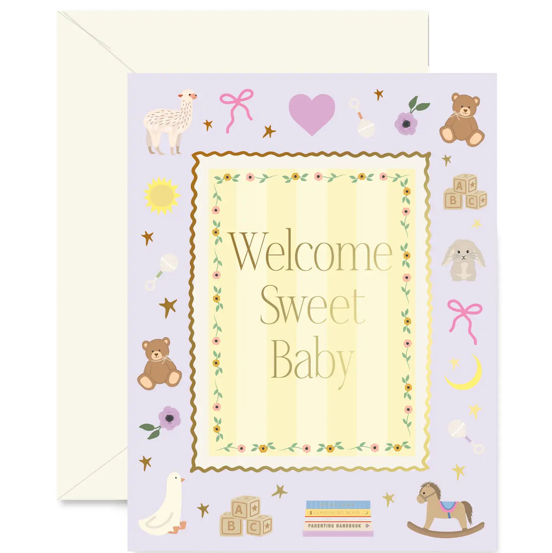 A baby shower greeting card with a pale lavender background and a cream envelope behind it. The card features the words 'Welcome Sweet Baby' in a decorative central frame, surrounded by cute illustrations of toys and nursery items including teddy bears, baby blocks, a rocking horse, a duck, and stars.