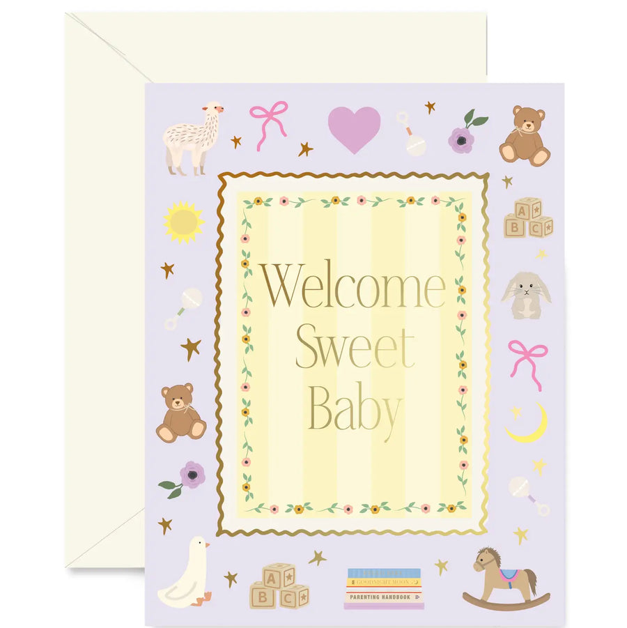 A baby shower greeting card with a pale lavender background and a cream envelope behind it. The card features the words 'Welcome Sweet Baby' in a decorative central frame, surrounded by cute illustrations of toys and nursery items including teddy bears, baby blocks, a rocking horse, a duck, and stars.