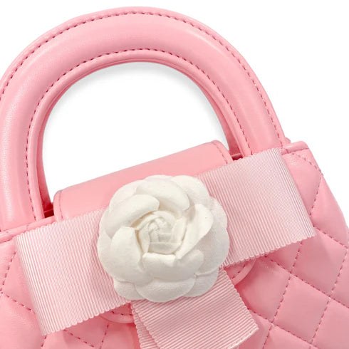 Close-up of a pink handbag with a white flower and ribbon detail on a white background