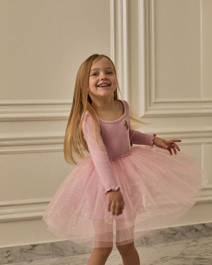 Young girl in a pink dress standing in a room with decorative walls.