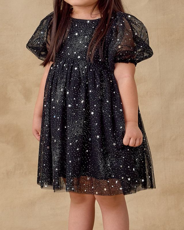 Child wearing a black dress with star patterns on a beige background