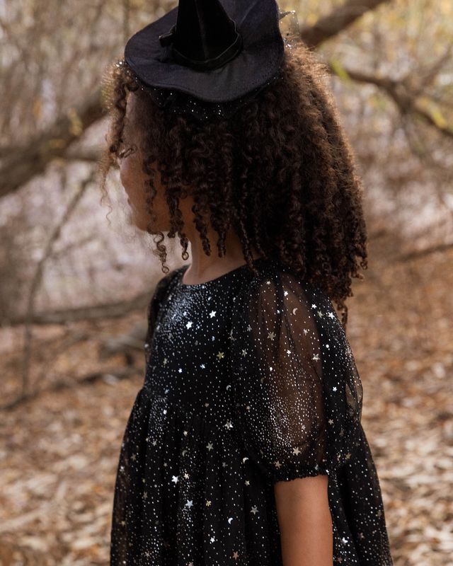 Child wearing a black witch hat and star-patterned dress outdoors.