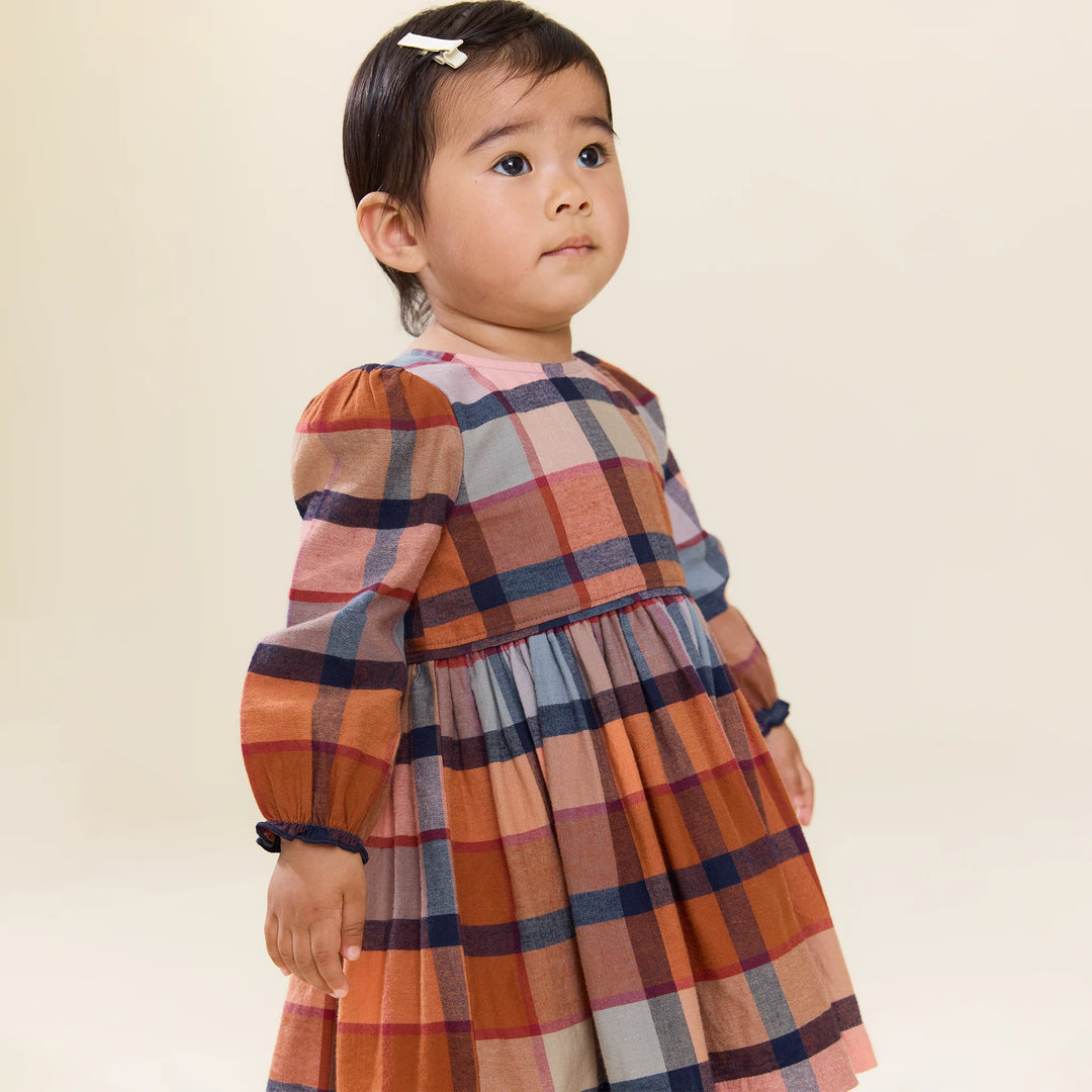 close up of the young toddler wearing the rust plaid dress. the sleeves come to her wrists here. 