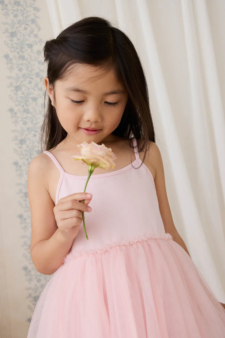 Young girl in a pink dress holding a flower against a light curtain background