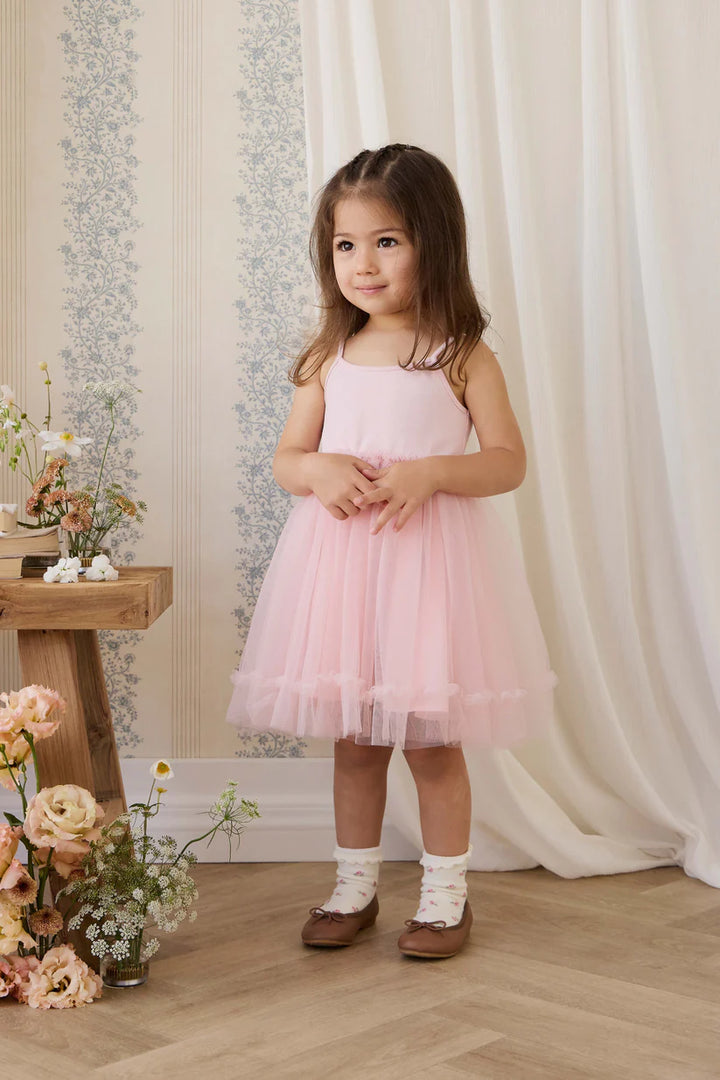 Young girl in a pink dress standing in a decorated room with flowers and curtains.