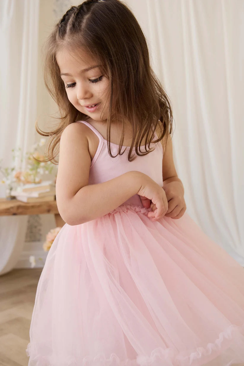 Young girl in a pink dress standing indoors with a neutral background