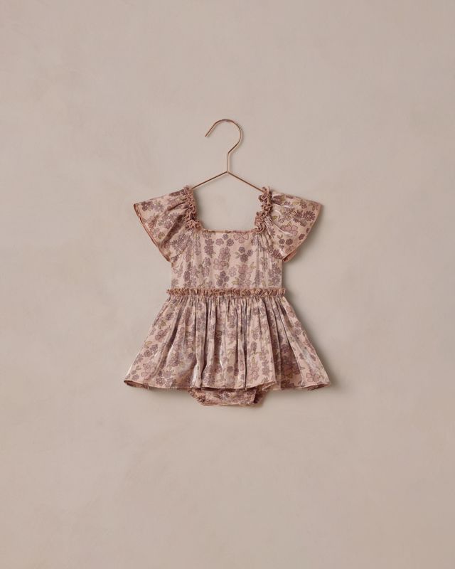 Floral-patterned baby romper on a hanger against a beige background