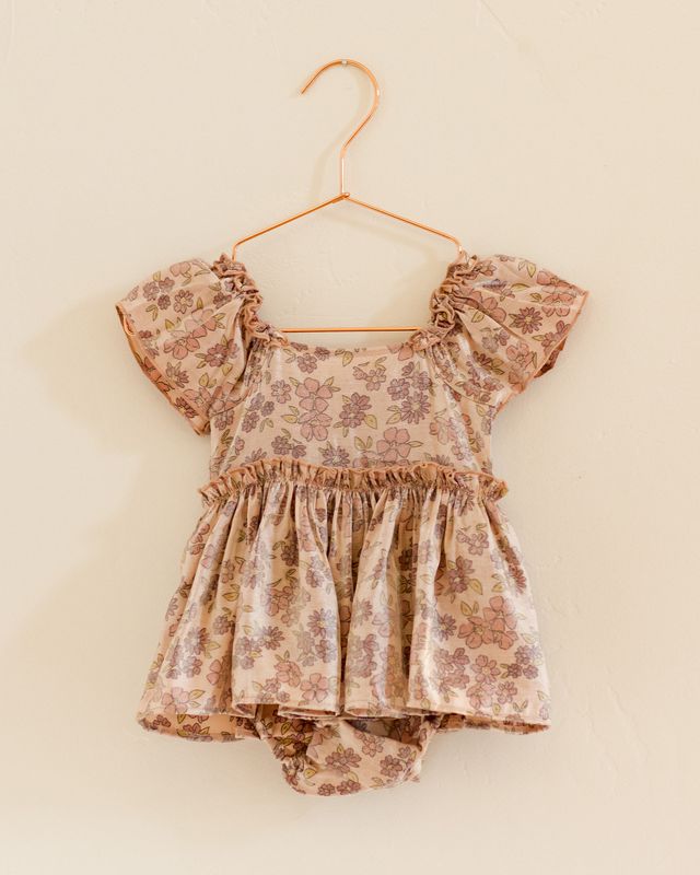 Floral baby romper on a hanger against a beige background