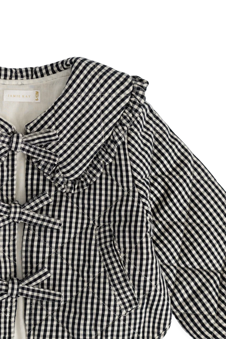 A close-up of a black and white gingham quilted jacket with ruffled collar and bow details, shown on a plain white background.