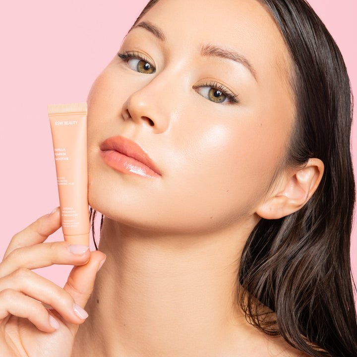 Woman holding a lip balm product against a pink background