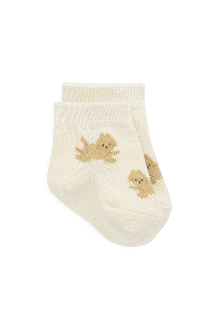 A pair of cream-colored baby ankle socks featuring small tan knit dog illustrations, displayed against a solid white background.