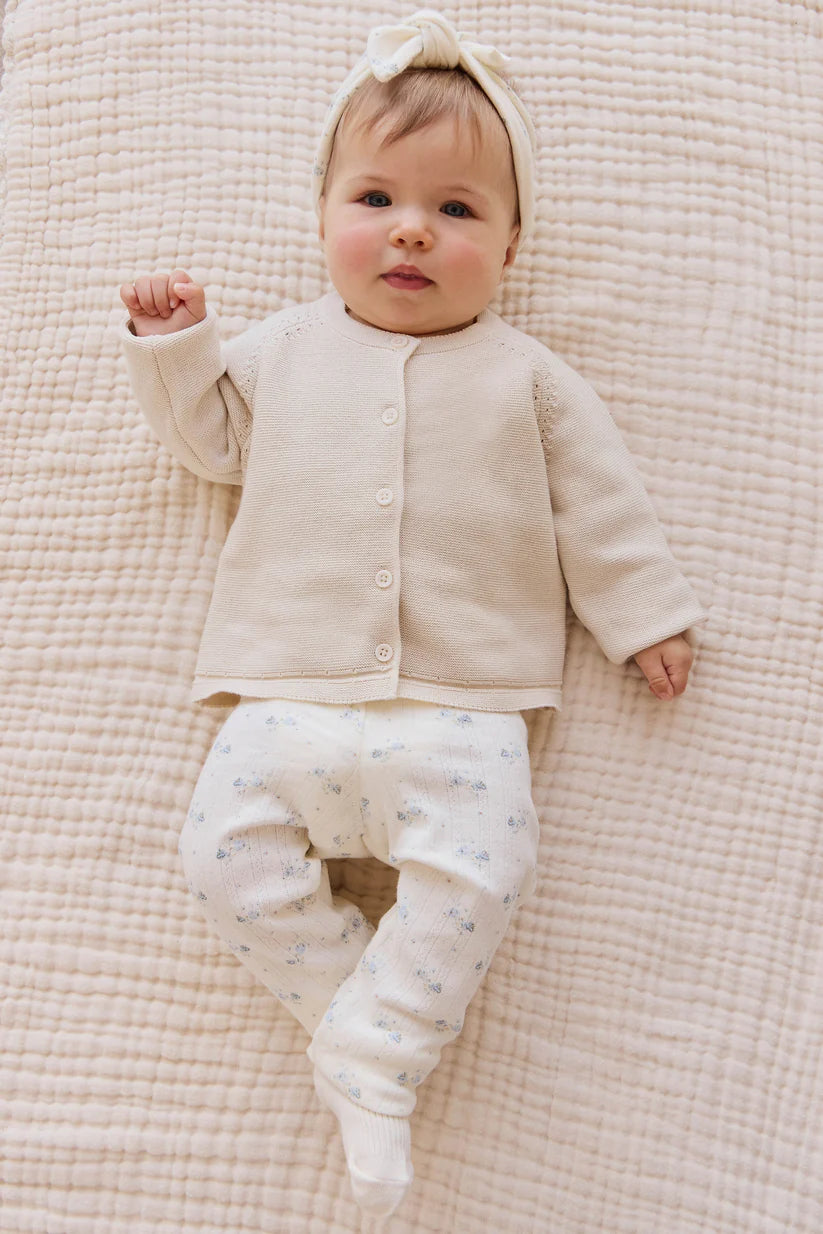 Baby in cream outfit lying on a textured beige blanket
