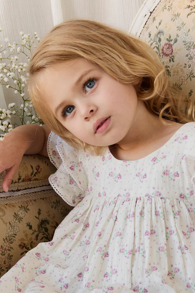 Young girl in a floral dress sitting on a floral-patterned couch.