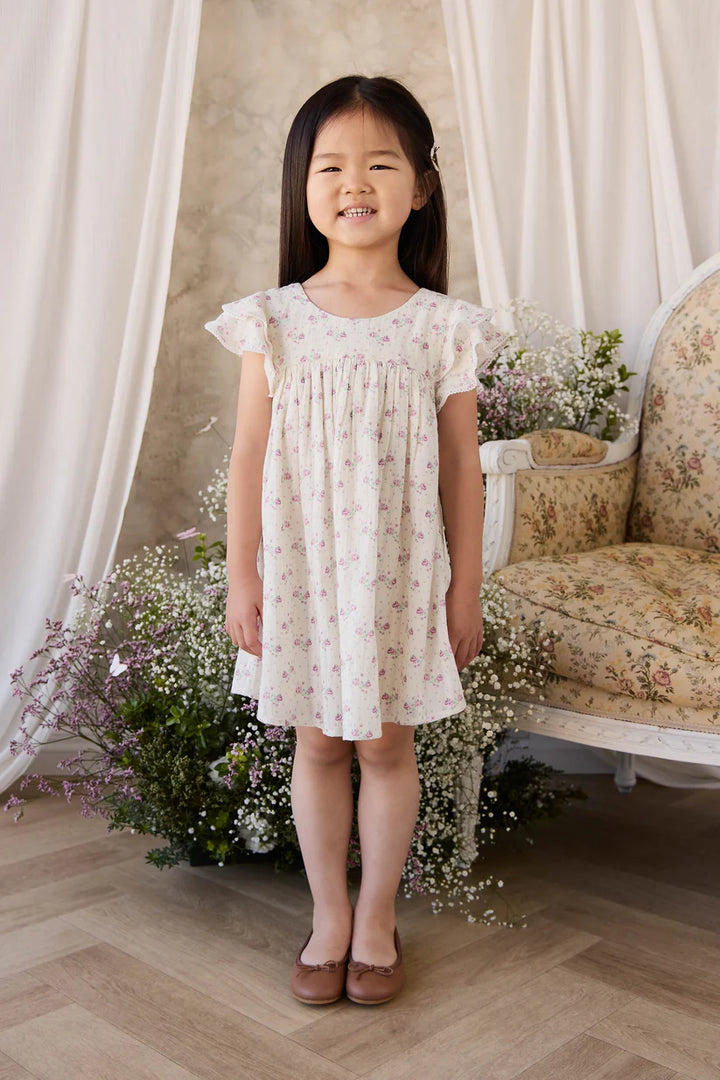 Young girl in a floral dress standing in a room with flowers and a couch.