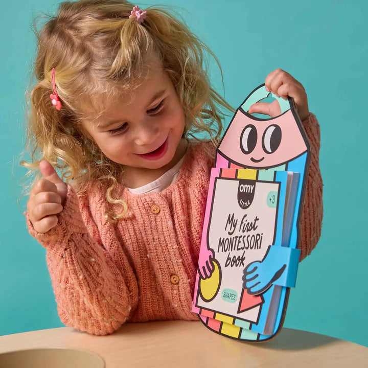 a child holding up a sticker book shaped like a pencil with rainbow colors 