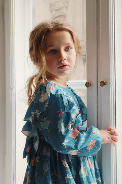 Little girl wearing dress and turned to the side so we can see the dress from a different point of view. you can see the drama of the ruffle from here