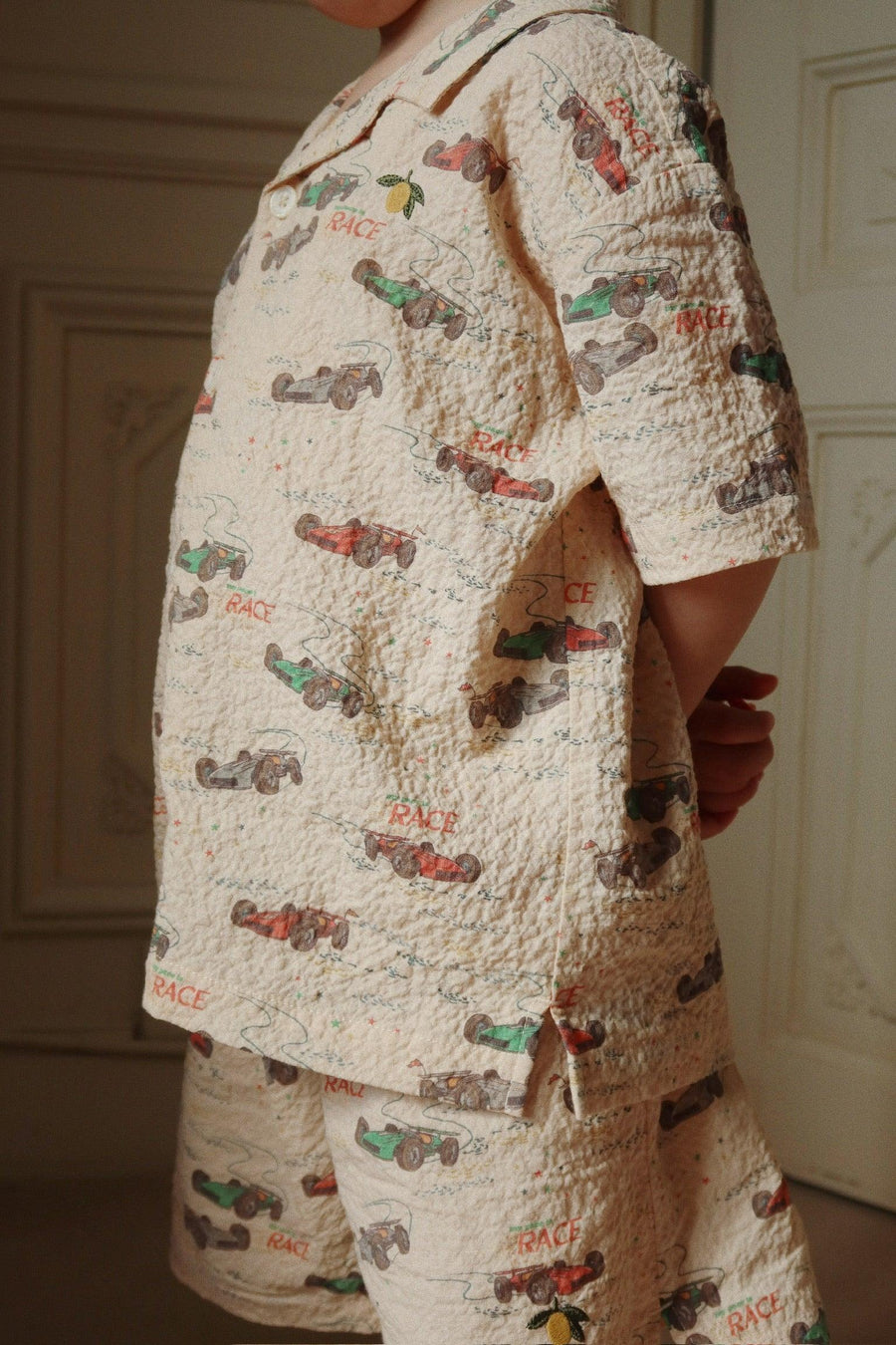 this is a picture of a boy modeling a two piece set with race cars all over the top and shorts. 