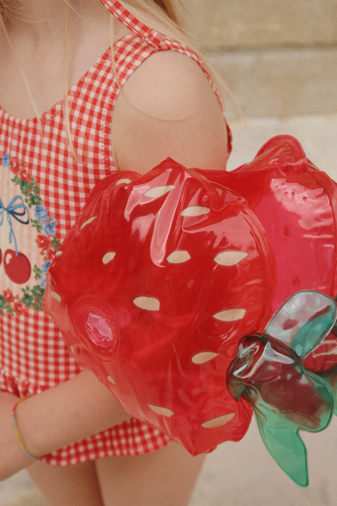 young child wearing water wings shaped like a strawberry. 