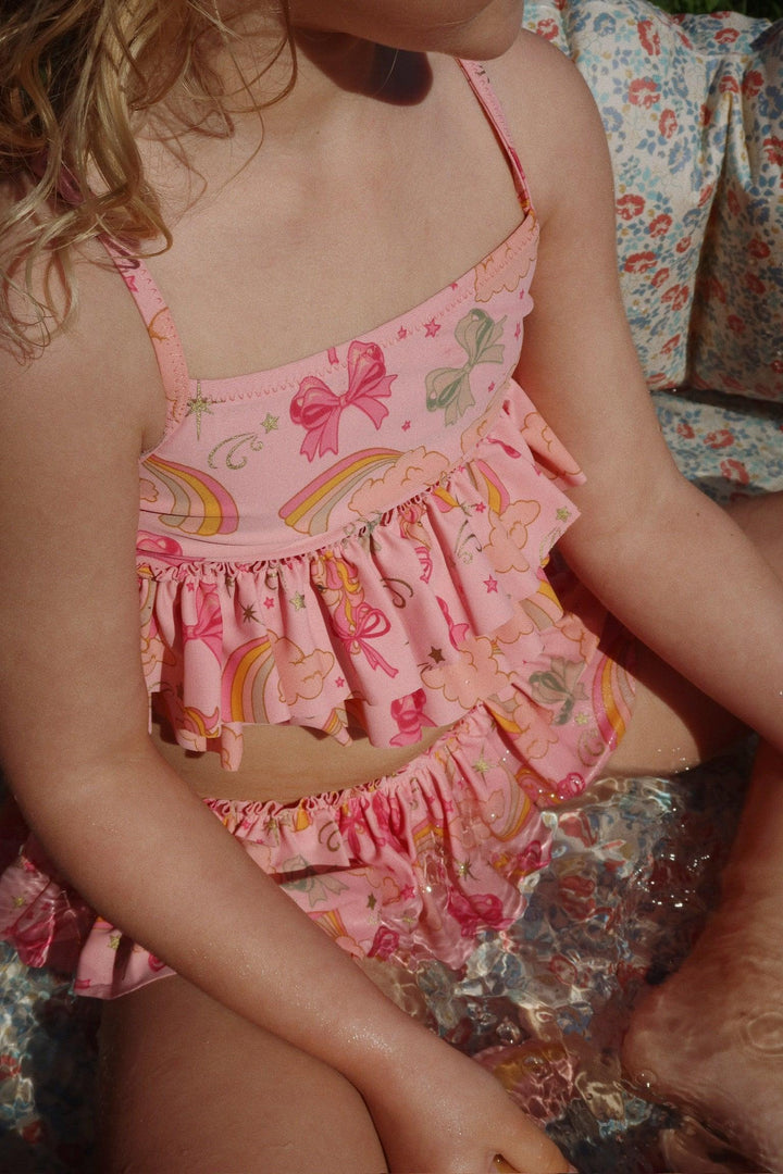 picture of little girl wearing the two piece bathing suit. pink in color with bows, rainbows and unicorns on it. 