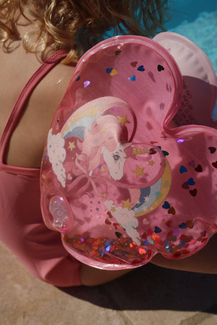 young child wearing pink water wings with unicorn and multi color glitter inside the water wings.