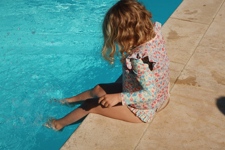 little girl sitting at the pool with her feet in the water . this shows the colors and print of the bathing suit in the daylight 
